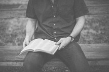 A man sitting on a bench reading the Bible