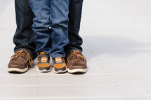 Legs and feet of a man and boy standing together.