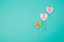 Three Valentine candy hearts on an aqua background.