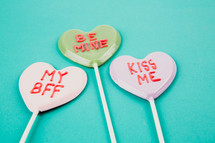 Candy hearts on a stick with Valentine messages on an aqua background.