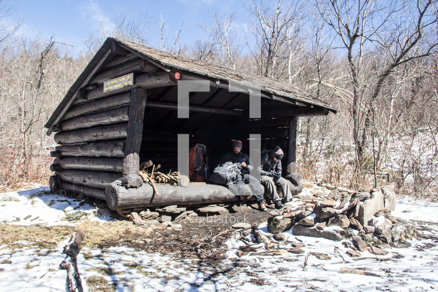 men on a hiking trail resting under a log shelter 