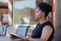 a woman sitting outdoors reading a Bible on a patio 