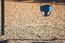 Child's bucket swing hanging over wood chips.