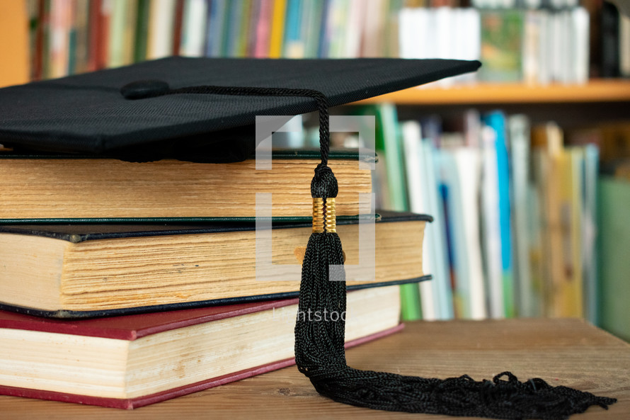 graduation cap on a stack of books on a desk in a library 
