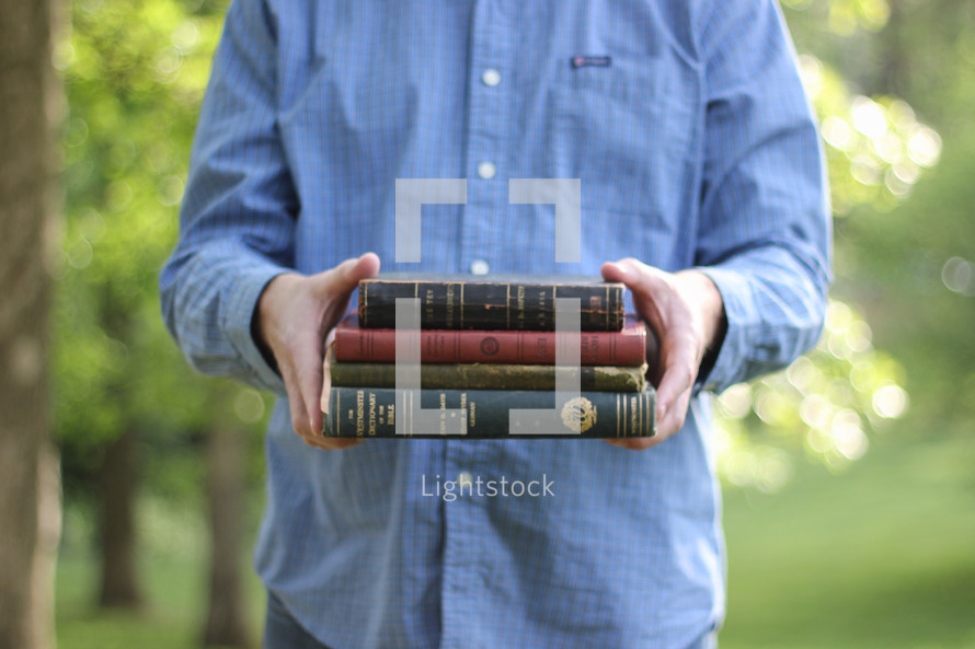 Man holding a stack of books outside.