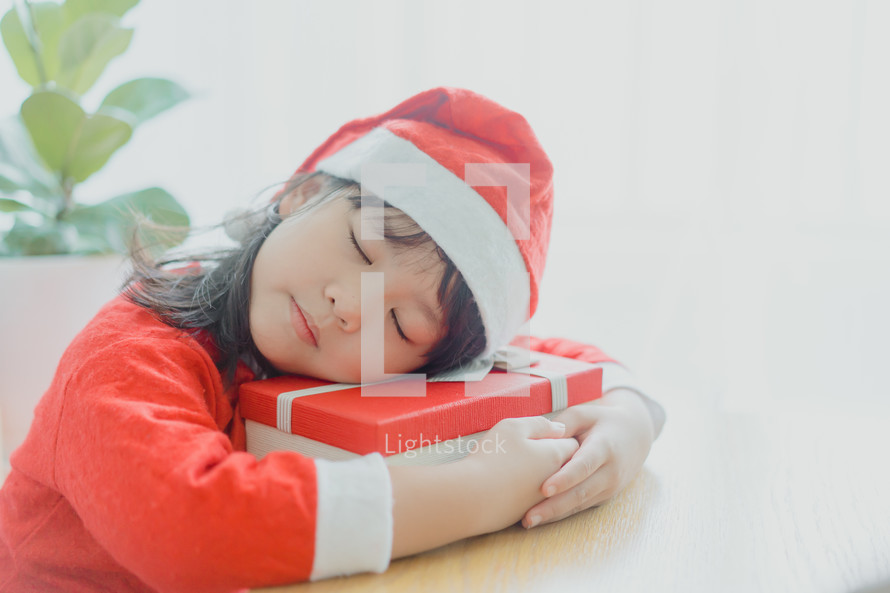 a little girl in a Santa suit sleeping on a Christmas gift 
