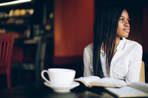woman with her head turned to the side sitting in front of a Bible and a coffee mug at a coffee house