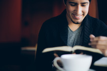 man reading from a Bible sitting in front of a coffee mug