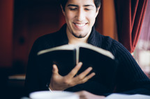 man reading a Bible and smiling at the Good News