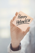 woman holding a sticky note with the words Happy Halloween 