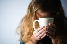 woman holding a mug of coffee with head bowed in prayer