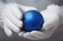 white gloves holding a blue ball ornament 