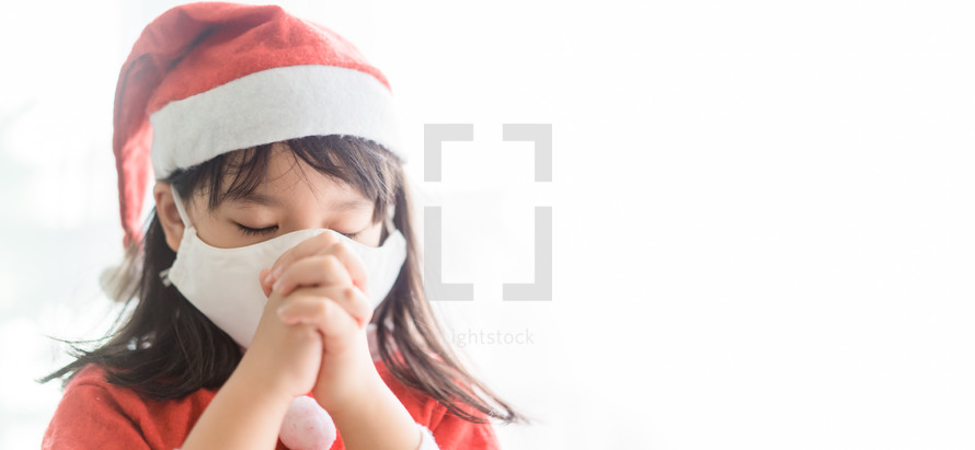 a little girl in a face mask and Santa suit praying