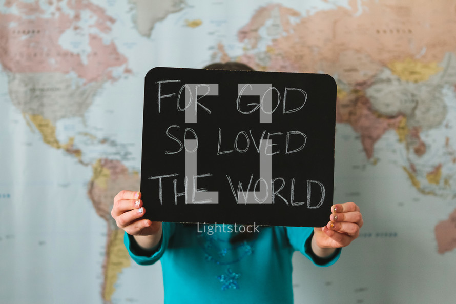 A girl in front of a world map holding a sign - For God so loved the world 