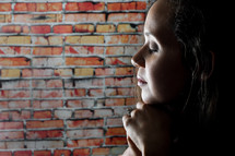 woman in prayer and a brick wall 