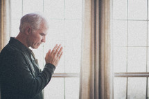 elderly man standing at a window in prayer