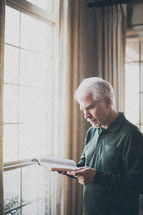 elderly man standing in front of a window Reading a Bible by sunlight