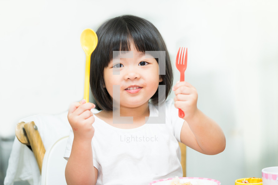a toddler eating holding a fork and spoon 