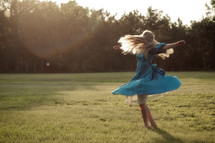 Girl twirling around outside in a field of grass.