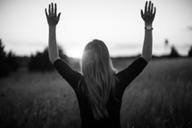 a woman standing in a field with hands raised 