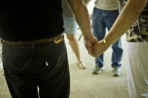 Men and women standing in a circle while holding hands.