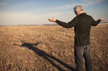 elderly man standing outdoors in a field with his arms outstretched in praise and worship to God