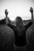 a woman standing in a field with raised hands