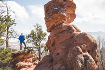 man standing on a red rock formation at the top of a mountain 