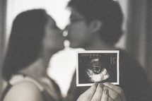 Kissing couple holding a sonogram picture.