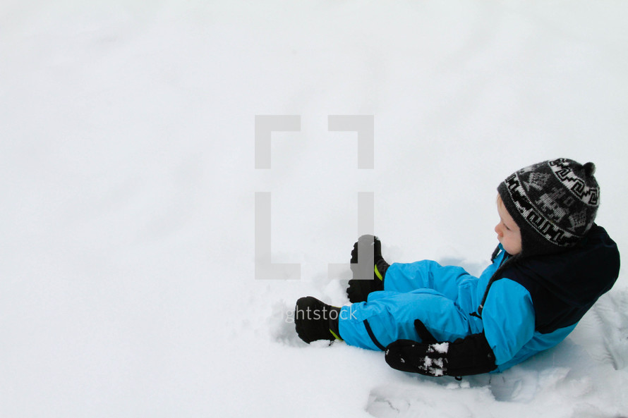 a toddler boy in a snowsuit sitting in snow 