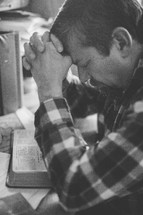 a man sitting at his desk praying and reading a Bible 