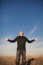 elderly man standing in a field with his arms outstretched in worship to God