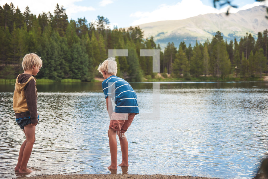 two boy standing on the shore of a lake 