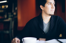 man with his head turned to the side sitting in front of a coffee mug and Bible