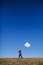 Man carrying white flag on grassy hilltop.