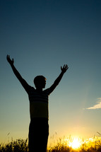 silhouette of a man with raised hands in worship at sunset 