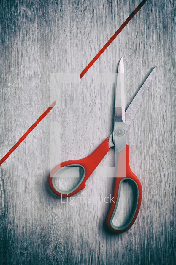 Bright red scissors cutting vibrant ribbon on wooden table, showcasing crafting creativity with touch of danger. Texture adds depth to visually appealing still life photo