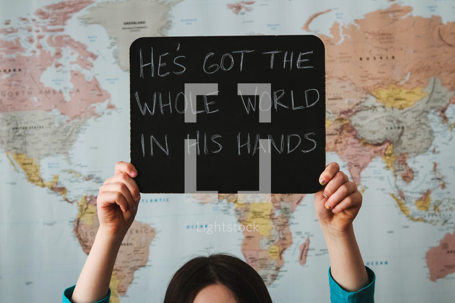A girl in front of a world map holding a sign - He's got the whole world in His hands 