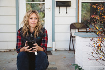 woman sitting on a stoop in front of her house holding a mug of tea 