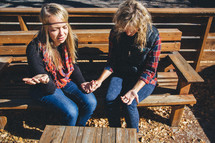 women sitting on a bench holding hands in prayer 