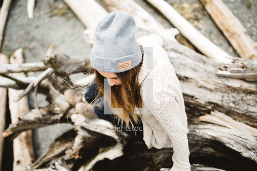 woman in a wool cap sitting on driftwood 