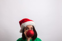 woman in an ugly Christmas sweater and santa hat hiding behind a Christmas ornament 