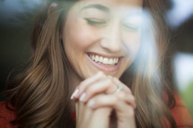 A smiling young woman with her hands clasped in prayer.