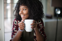 A smiling young woman holding a coffee mug.