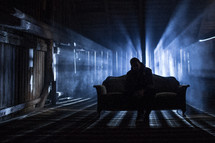 man sitting on a couch in a dark room alone 