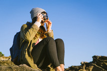 woman sitting on rocks taking pictures with a camera 