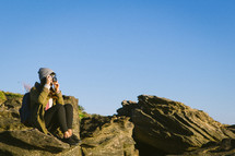 woman sitting on a rock taking pictures with a camera 