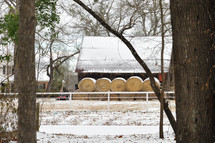stacked hay bales in front of a barn in the snow 