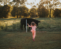 girl running towards a cow in a pasture 