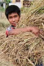 a young man carrying a bundle of hay 